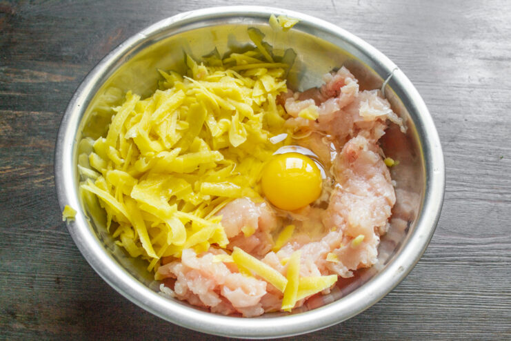 Добавление куриного яйца к картофелю и фаршу в миске