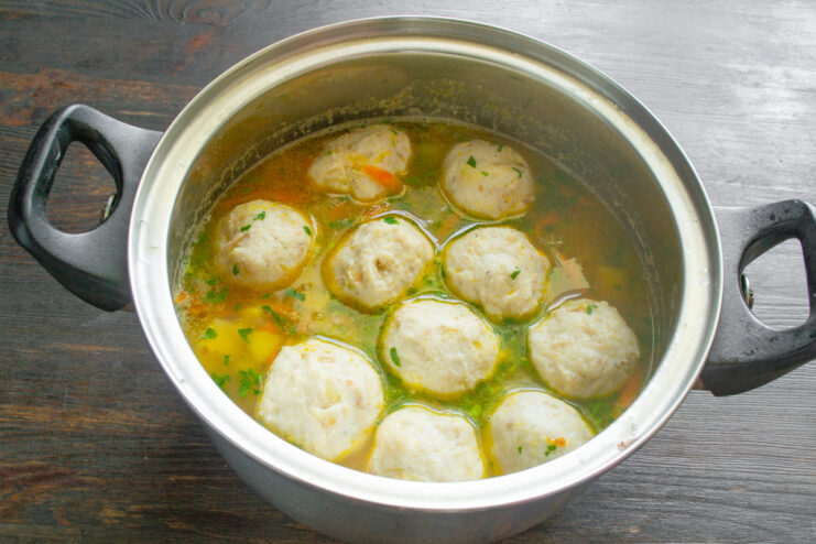 Готовый куриный суп с фрикадельками и зеленью в кастрюле