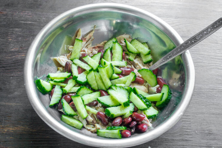 Нарезанные свежие огурцы в миске с курицей и фасолью