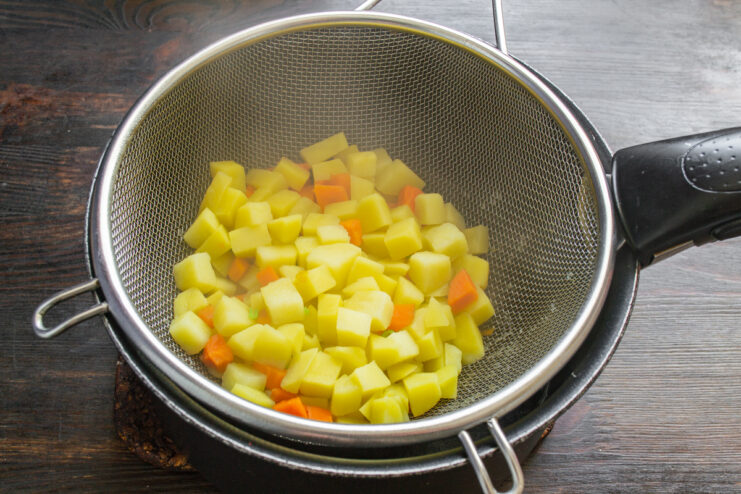 Отваренные кубики картофеля и моркови в сите