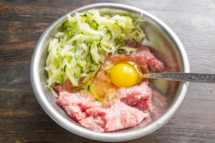 Добавление куриного яйца и соли в мясной фарш с кабачком