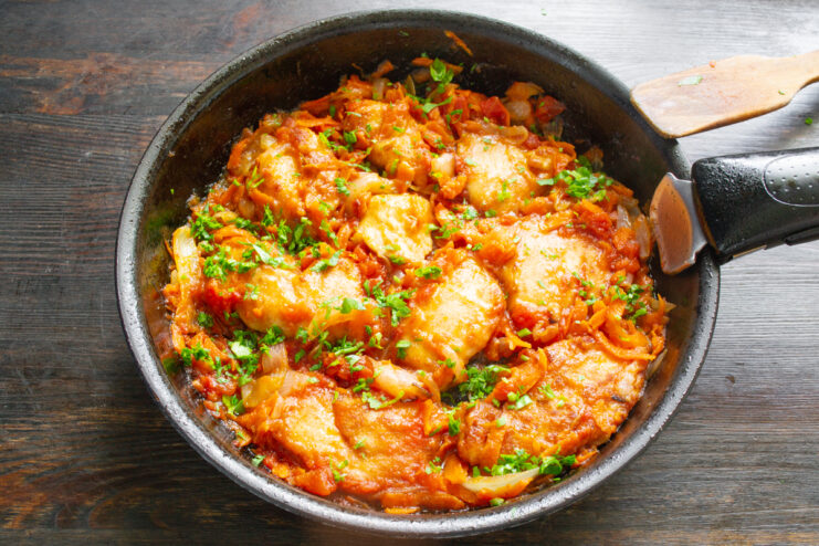 Готовая сочная куриная грудка с овощами в сковороде, посыпанная свежей петрушкой
