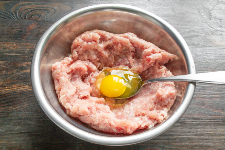 Добавление яйца в фарш Куриное яйцо, разбитое в миску с куриным фаршем