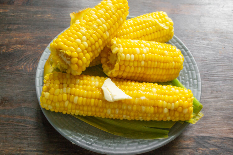 Смазывание кукурузы сливочным маслом Кусочек сливочного масла тает на горячем початке кукурузы