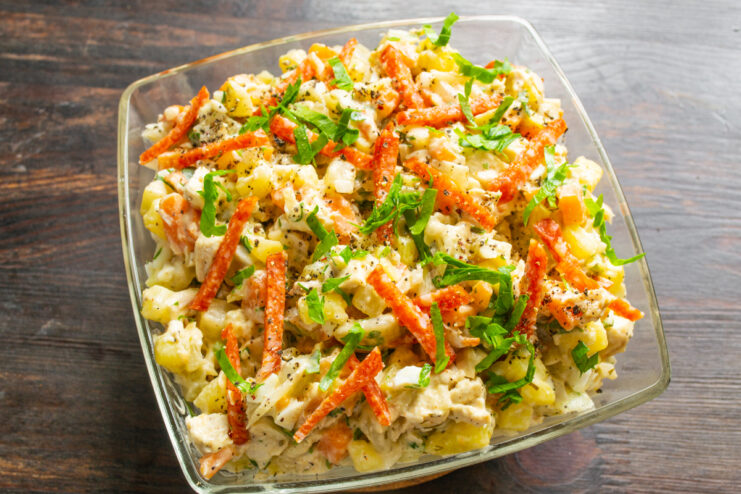 Столичный салат с курицей и копченой колбасой в салатнике, вид сверху
