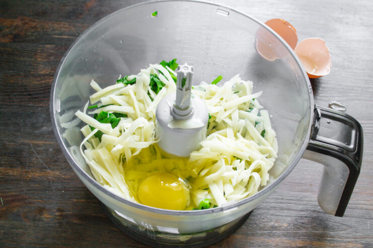 Сырое яйцо в чаше комбайна с кабачками, шпинатом и сыром