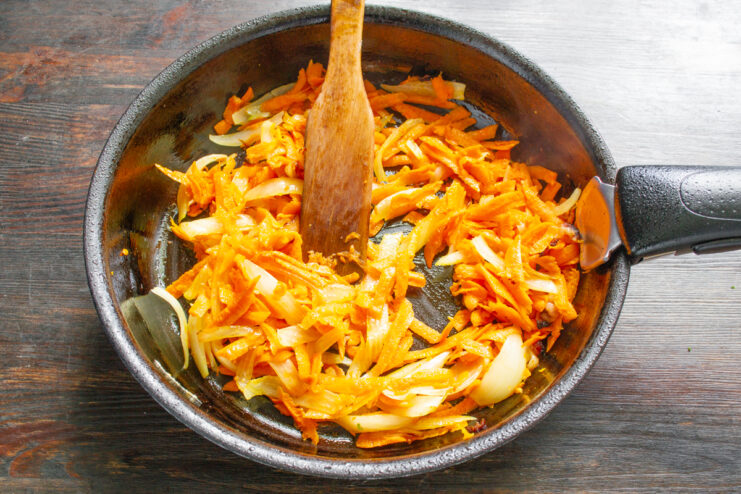 Тертая морковь, тушенная с луком и беконом на сковороде